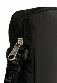 Borsa in tessuto nera con zip argentata e tirazip in metallo, tracolla testurizzata e cuciture sottili lungo i bordi. Forma rettangolare compatta.
