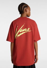 Camiseta de algodón roja con corte holgado y mangas cortas. Presenta un gran gráfico del logotipo amarillo de Vans en la parte posterior. Textura suave.