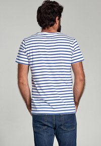 Witte t-shirt met korte mouwen en horizontale blauwe strepen, met een ronde hals en een ontspannen pasvorm. Gepaard met donkerblauwe jeans.