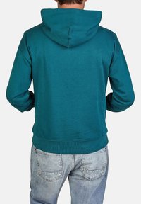 Sudadera verde azulado con un bolsillo tipo canguro y capucha con cordón, confeccionada en una tela suave. Presenta puños y dobladillo de canalé, combinada con jeans de color azul claro.