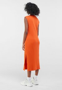 Robe midi orange côtelée avec une fente au dos, sans manches et à col montant, associée à des baskets blanches chunky et des chaussettes montantes.