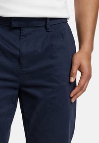 Pantaloni blu navy realizzati in materiale liscio, caratterizzati da un davanti piatto, passanti per la cintura e una vestibilità comoda. Tasche laterali rinforzate visibili.