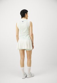 Top atlético sem mangas verde-claro com gola redonda, combinado com uma saia plissada. Feito de tecido suave, com um logotipo em relevo na parte de trás.