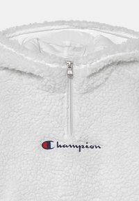 Felpa con cappuccio in pile di colore grigio chiaro con chiusura a mezzo zip. Presenta una superficie texturizzata e il logo "Champion" ricamato in blu navy e rosso.