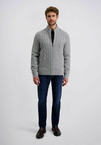Grauer Strickcardigan mit Kabelmuster, Reißverschluss vorne und hohem Kragen. Kombiniert mit dunkelblauen Jeans und dunklen Schuhen. Glatte Textur.