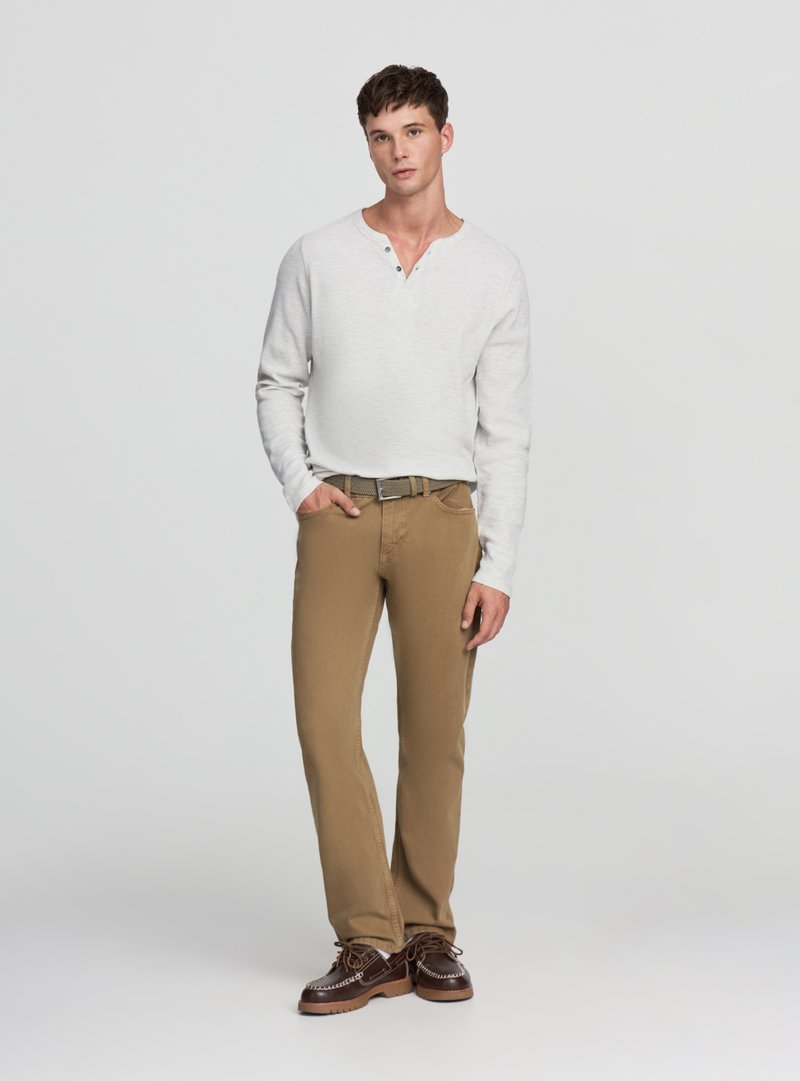 Maglietta henley a maniche lunghe grigio chiaro con tre bottoni, abbinata a pantaloni chinos color sabbia a gamba dritta e scarpe marroni con lacci. Vestibilità strutturata e trama visibile.