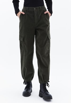 Pantaloni cargo verde oliva con vita elasticizzata, tasche laterali e caviglie rimboccate, abbinati a stivali da combattimento neri con lacci.