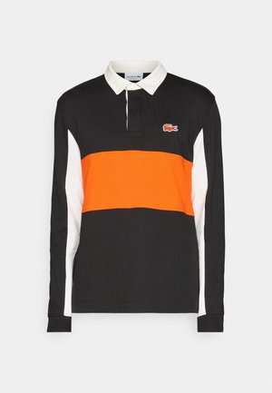 Chemise de rugby noire à manches longues avec col blanc, rayures blanches sur les manches et une bande horizontale orange traversant la poitrine avec un logo de crocodile.
