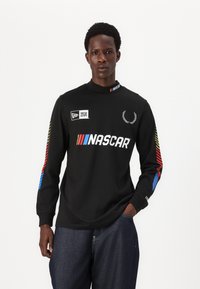 Svart langermet skjorte med NASCAR-logo, og fargerike striper på ermene (rød, gul, blå) samt høy hals.