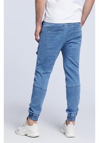 Pantalones jogger en azul claro, confeccionados en una mezcla de algodón, con puños elásticos, bolsillos laterales y una textura desgastada, combinados con zapatillas blancas.