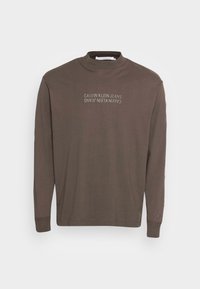 Brun långärmad t-shirt med hög krage, med en tonad logotryck på framsidan. Mjuk tyg och åtsittande ärmslut.