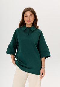 Donkergroene, oversized poloshirt van zachte stof met een platte kraag en korte mouwen, voorzien van een drieknopenfront en een relaxte pasvorm.