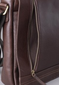 Brown leather bag with a textured finish, featuring a metal zipper and contrasting stitching. The interior is lined with a soft fabric.
