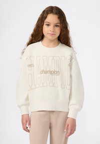 Sudadera color crema hecha de una tela suave, con un gran texto "CHAMPION" en beige en el frente y puños acanalados.