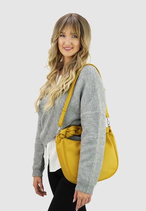 Gele leren hobo-tas met knoopaccent. Voorzien van een stevige riem en een gestructureerd oppervlak. Draagt een grijze trui en zwarte broek.