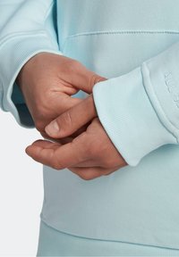 Sweat-shirt bleu clair avec poignets côtelés. Gros plan sur des mains jointes, mettant en valeur la texture du tissu et les détails des coutures.