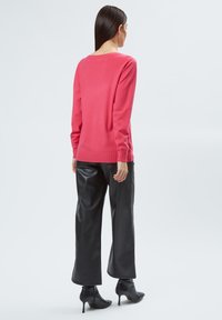 Roze gebreide trui met lange mouwen, gecombineerd met zwarte neplederen broek met wijde pijpen en zwarte hoge enkellaarsjes. Soepele textuur, eenvoudig ontwerp.