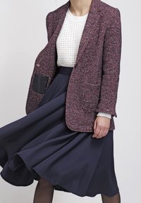 Texturovaný blazer v růžové a fialové barvě s dvěma předními kapsami, nošený přes bílý pletený svetr a splývavou námořnickou sukni.