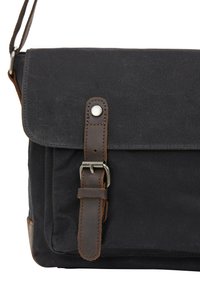 Canvas messenger taske i mørkegrå med brune læderdetaljer, der har en klaplukning og en rem med en metalspænde til justering.
