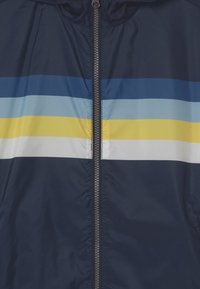 Námořnická bunda na zip s vodorovnými pruhy v světle modré, modré, žluté a bílé barvě. Hladká textura, kapuce a kovový zip.