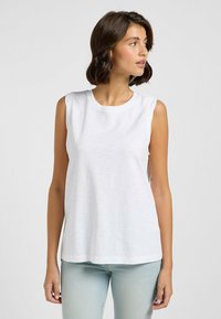 Camiseta sin mangas blanca en una tela ligera y suave. Presenta un escote redondo y un corte relajado. Marca sutil en la parte delantera.