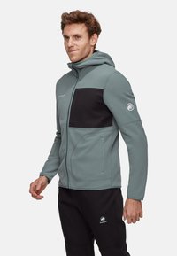 Hoodie aus Fleece in Hellgrau mit schwarzem Design-Panel, Reißverschlusstaschen und erhabenem Logo am Ärmel. Weiche Textur und enganliegendes Design.