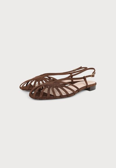 Sandales plates marron avec plusieurs brides fines et une petite boucle sur la bride de cheville, présentées sur un fond blanc.