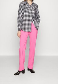 Chemise à manches longues à carreaux noirs et blancs, associée à un pantalon droit rose vif. Le mannequin porte des chaussures à talons noires brillantes.