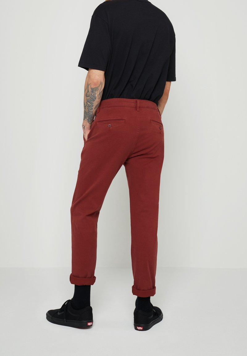 Pantaloni di cotone rossi con taglio affusolato, orli arrotolati e due tasche posteriori. Abbinati a una maglietta nera e sneakers nere.