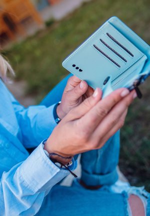 A mint green phone wallet made of textured material, featuring multiple card slots and a secure closure, held in hands.