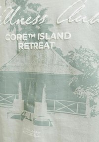 Κείμενο «CORE™ ISLAND RETREAT» με ξεθωριασμένο φόντο μια καλύβα με ψάθινη στέγη, δύο ξαπλώστρες, φοίνικες και βλάστηση.