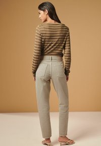 Haut à manches longues marron rayé, pantalon gris clair avec poches arrière et sandales légères. Texture lisse ; coupe douce et décontractée. Détails de design subtils.