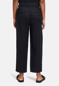 Pantalons large en lin noir avec une coupe décontractée, dotés de poches arrière et d'une texture lisse. Assortis à des sandales plates.