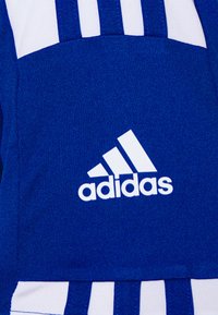 Prenda deportiva azul con tejido texturizado, detalles en blanco, tres franjas verticales y el logo de Adidas en una posición destacada.