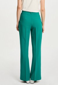 Groene wijde broek met een soepele textuur, hoge taille, subtiele achterzak en afgewerkt met zilveren schoenen.