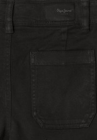 Svarta jeans i denim med bakficka och synliga sömmar. Har en svart etikett med vit text vid midjebandet. Slät textur.