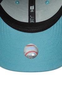Baseball kapa s tirkiznom pamučnom vanjskom dijelu, crnim vizorom i srebrnom metalnom oznakom s dizajnom bejzbol lopte i MLB brandom.