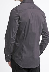 Mörkgrå långärmad skjorta med en slät textur, spetsig krage och knappade manschetter. Har en rundad fåll och en skräddarsydd passform.