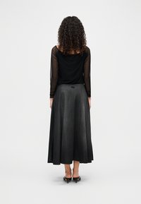 Μαύρο μακρυμάνικο τοπ από διαφανές ύφασμα, συνδυασμένο με σκουρόχρωμη φούστα Α γραμμής από τζιν ύφασμα, με σφηκοφωλιά στη μέση και ρέον σιλουέτα. Τακούνια ολοκληρώνουν την εμφάνιση.