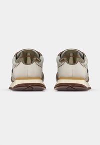 Joggesko med lys beige overdel, mørke detaljer og en brun gummisåle. Har en blank tung og merkevareløs hældetalj.