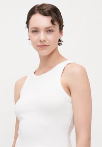 Weißes, geripptes Tanktop mit rundem Halsausschnitt und breiten Schulterträgern. Die glatte Textur und das enganliegende Design betonen die Körperkontur.
