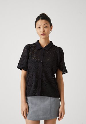 Blouse en dentelle noire à manches courtes et col. Dotée d'une fermeture boutonnée sur le devant et de motifs floraux délicats sur l'ensemble.