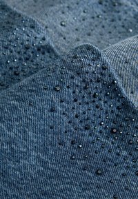 Dunkelblauer Denim-Stoff mit erhabenen schwarzen Pailletten, die in einem gepunkteten Muster über die Oberfläche verteilt sind und so Textur und visuelles Interesse erzeugen.