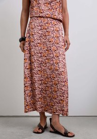 Vestido maxi con un patrón de olas en rosa, naranja y púrpura, hecho de una tela suave. Se combina con sandalias marrones con tachuelas.