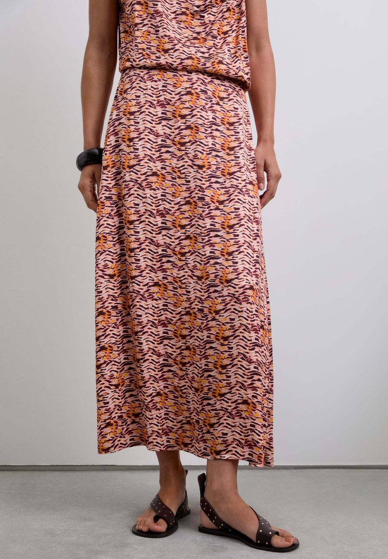 Vestido maxi con un patrón de olas en rosa, naranja y púrpura, hecho de una tela suave. Se combina con sandalias marrones con tachuelas.