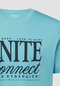 Light blue crew neck t-shirt with black text reading "MORE - LESS IS BORE UNITE Connect SYNERGIZE!" and s.Oliver branding inside collar.