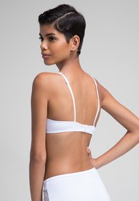 Sujetador blanco con tirantes delgados ajustables y un cierre de gancho y ojal en la parte posterior. Textura suave y diseño ajustado.