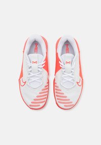 Zapatillas deportivas blancas con detalles en coral, que cuentan con una parte superior de malla texturizada, cierre de cordones y un patrón distintivo en la suela.