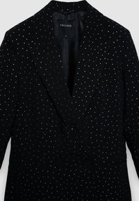 Schwarzer, doppelt geknöpfter Blazer mit silbernen Verzierungen, ausgestattet mit spitzem Revers, strukturiertem Stoff und zwei Fronttaschen.