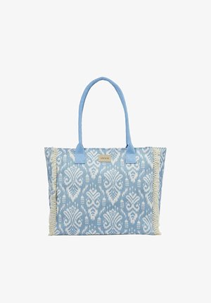 Bolso tote con estampado azul y blanco con flecos en los laterales y dos asas largas azules para llevar al hombro.